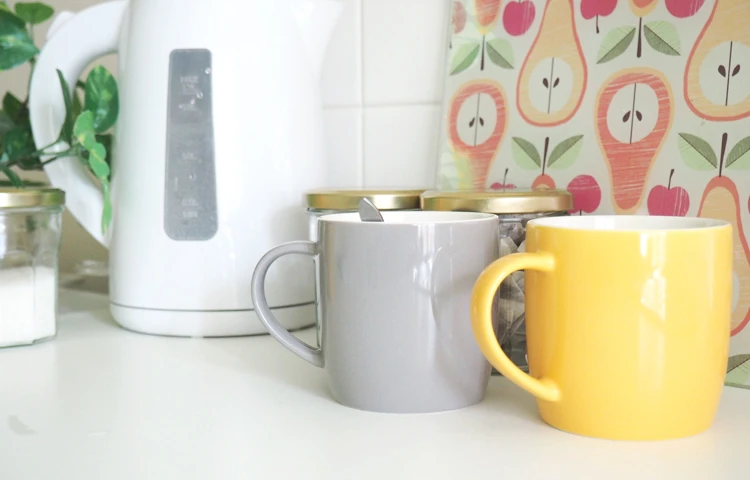Yellow and grey mugs sat beside a kettle in Abbeyfield House