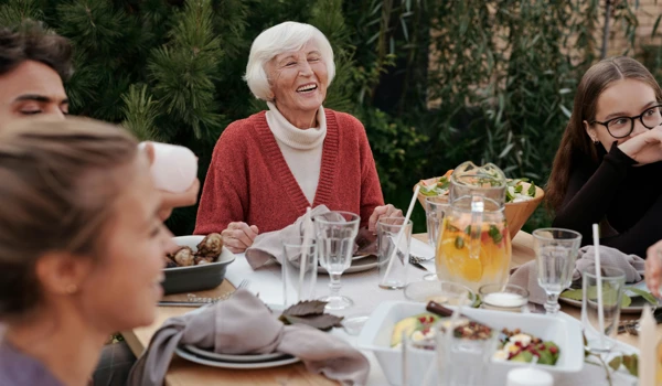 Older Woman With Family And Friends Eating Round The Table Together