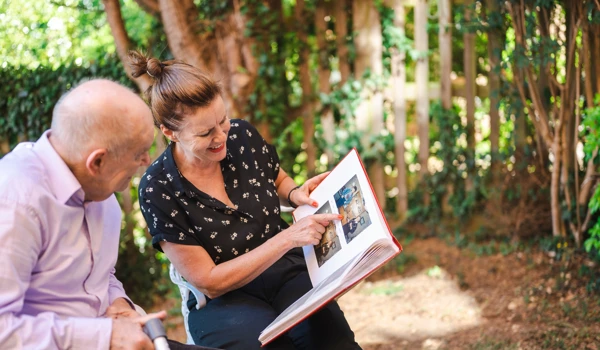 Woman And Older Man Sitting In Garden Looking Through Photo Album